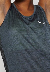 Tmavě šedý sportovní top bez rukávů s hladkou texturou, kulatým výstřihem a jemným logem na levé straně hrudi. Prodyšný postranní panel.