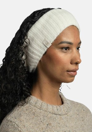 White ribbed headband made of soft material, featuring a small branded tag on the side. Curly hair visible underneath.