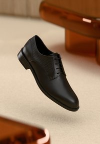 Μαύρα δερμάτινα παπούτσια με λείο φινίρισμα και υφασμάτινες λεπτομέρειες. Κλασικός σχεδιασμός με κορδόνια, στρογγυλερή μύτη και χαμηλό τακούνι.
