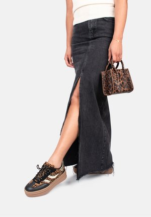 Kvinde iført en sort denimnederdel med frontslids og leopardprintede sneakers, der holder en matchende leopardprintet håndtaske.