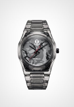 Montre grise transparente avec cadran à motif camouflage, aiguilles noires et rouges, et bracelet à maillons transparent assorti.