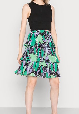 Femme portant un crop top noir sans manches et une jupe multi-couches avec un motif floral abstrait vert, violet, noir et blanc.