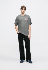 Gaišpelēka kokvilnas T-krekle ar īsām piedurknēm un grafisku drukājumu ar sarkaniem un ziliem elementiem. Apvienota ar melnām plati grabēcām biksēm un ziliem apaviem.