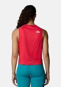 Top deportivo sin mangas rojo con un acabado texturizado, que presenta un logo en la parte posterior. Combinado con leggins ajustados de color teal.