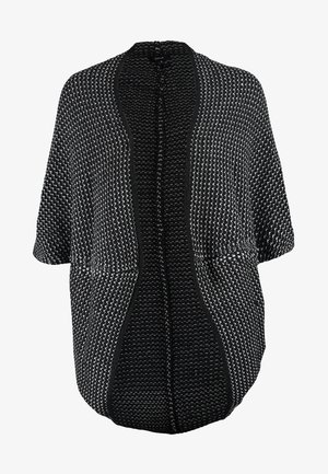 Kvinde iført sort- og hvidmønstret sjal, hvid top, sorte bukser, sorte støvler med hæl, bærende på en stor sort håndtaske, mens hun går.