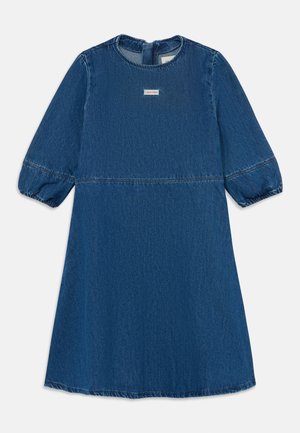 Džinsu kleita dziļi zilā krāsā ar apaļu apkakli, pūkainām piedurknēm un izteiksmīgu šuvju līniju jostasvietā. Priekšpusē ir redzama zīmola birka.