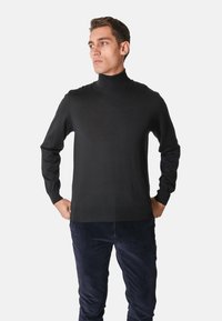 Maglione a collo alto nero in un tessuto morbido, con maniche lunghe, design aderente, collo e orlo a coste, abbinato a pantaloni di velluto a coste blu navy.