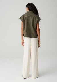 Olijfgroene top met korte mouwen en een gestructureerd bladvorm patroon, gecombineerd met losse, crèmekleurige wijde broek.