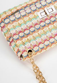 Woven handbag in cream, pink, blue, and gold, featuring a patterned exterior, gold hardware, and a detachable chain strap.