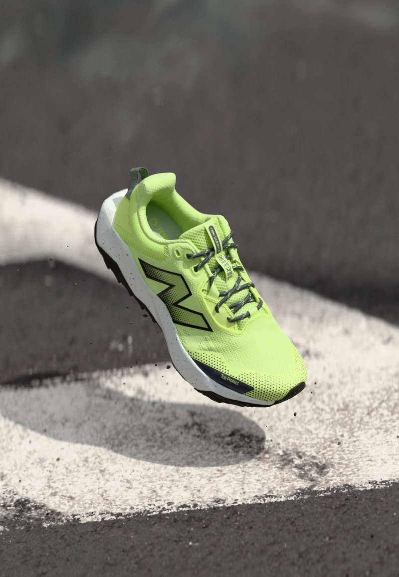 Neon green running shoe with a textured mesh upper, black detailing, and a white speckled sole. Features reinforced toe protection.