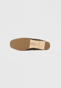 Καφέ παπούτσι από σουέτ με επίπεδη, ταμπά λαστιχένια σόλα. Διαθέτει ραφές κατά μήκος των άκρων και ένα μικρό λογότυπο στη σόλα. Ελαφρώς στρογγυλεμένο σχήμα μύτης.