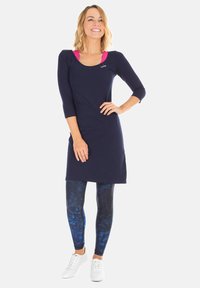 Abito navy con scollo rotondo e maniche a tre quarti, abbinato a leggings blu con motivo e sneakers bianche. Tessuto a trama liscia.
