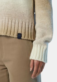 Strickpullover mit einem Farbverlauf von Beige zu Creme; gerippte Bündchen und Saum; kleines Logotag am unteren Ende. Kombiniert mit beigefarbenen Hosen.