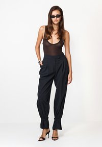 Pantaloni negri cu talie înaltă, cu pliseuri, cu glezne taperizate, asociați cu un body transparent negru și ochelari de soare negri. Material moale, design formal.