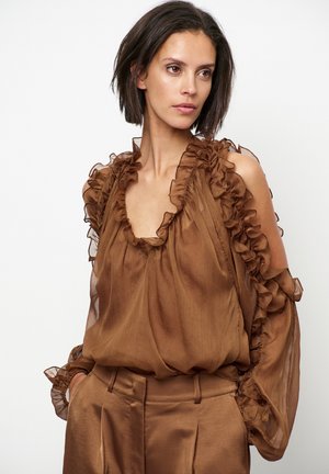 Bruine chiffonblouse met gerimpelde halslijn en mouwen, met een losse pasvorm en een ontwerp met blote schouders, gecombineerd met bijpassende bruine broeken.