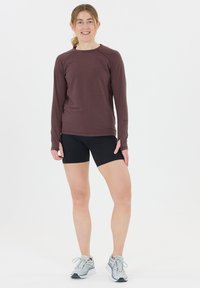 Langærmet maroon atletisk top kombineret med sorte shorts og grå løbesko. Glat stof med en tætsiddende design, der har minimale sømme.