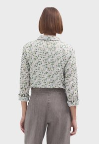 Camisa recortada en un tejido ligero, con un fondo blanco y patrones abstractos en verde y amarillo; mangas con vuelta y detalle en el collar.