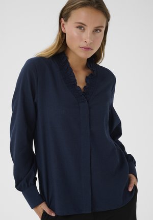 Blusa de manga larga azul marino con cuello volante, escote en V y cierre de botones. Tejido texturizado con sutiles líneas verticales. Corte holgado.