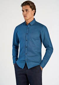 Langsleevige, knoopsluiting shirt in donkerblauw, gemaakt van zachte stof. Bevat een kraag, knopen aan de voorkant en een getailleerd ontwerp. Gecombineerd met donkere broek.