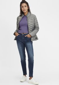 Chaqueta acolchada gris, top recortado a rayas, jeans azul oscuro y zapatillas blancas. La chaqueta tiene un cuello alzado y una textura acolchada.