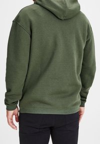 Olivgrüner Hoodie mit großer Kapuze, gerippten Bündchen und geradem Saum; aus weichem Material mit glatter Textur gefertigt.