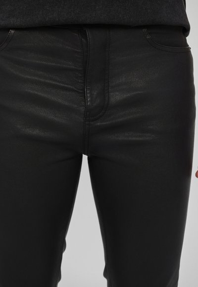 Zwarte neplederen skinny jeans met een gladde textuur, voorzien van gestikte naden en traditionele zakken. Strak aansluitend ontwerp voor een slank uiterlijk.