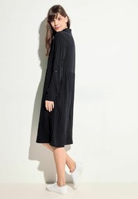 Abito tunica nero con texture a righe verticali, collo a camicia, maniche lunghe e una vestibilità comoda, abbinato a sneakers bianche.