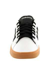 Sneaker bianca con accenti neri, caratterizzata da una suola in gomma, lacci neri e una linguetta nera texturizzata. Logo Adidas visibile sulla linguetta.