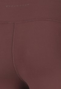 Vinröda sportleggings med en slät textur, elastiskt material och kontrasterande sömnadsdetaljer. Logotyp synlig nära midjebandet.