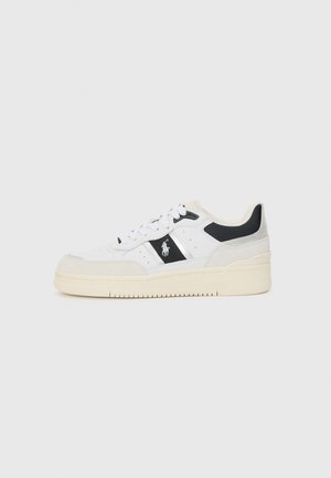 Hvit sneaker med svarte detaljer, laget av semsket skinn og lær, snøring foran, tykk kremfarget såle og en logo på siden.