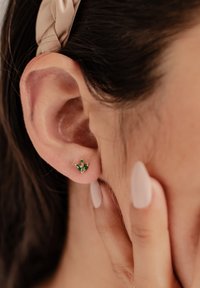 Grüne Edelsteinohrstecker in Blattform, mit drei marquisegeschliffenen Steinen und einem runden Akzent. Auf einer goldfarbenen Basis montiert.