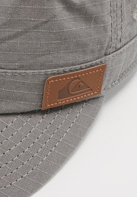 Sombrero de cubo de tela gris con una superficie texturizada, detalles cosidos y un parche de cuero marrón con un acento de logo.