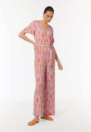 Patterned jumpsuit featuring a V-neck, short sleeves, a belted waist, and a fluid, wide-leg design in pink, orange, and lavender tones.