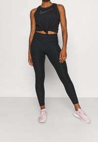Czarny sportowy crop top z supłem u dołu, zestawiony z czarnymi legginsami w wzory i jasnoróżowymi sneakersami. Nowoczesny design z eleganckimi liniami.