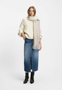 Læderstrik med grov kabelstrik, lys beige tørklæde, knælang denimnederdel med slids foran og sorte hælede ankelstøvler med detaljer.