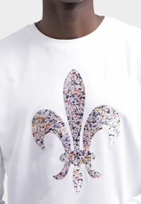 Bílé bavlněné tričko s velkým stylizovaným vícebarevným motivem fleur-de-lis s texturovaným uměleckým vzorem.