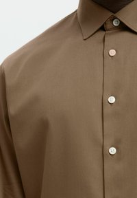 Καφέ πουκάμισο με κουμπιά, φτιαγμένο από λεία ύφασμα, με διπλωμένο γιακά και τρία κουμπιά σε διάφορες αποχρώσεις, με κομψή σχεδίαση.