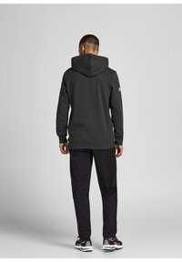 Sudadera gris con capucha y puños y dobladillo acanalados, combinada con pantalones oscuros y zapatillas deportivas multicolor, vista desde la parte de atrás.