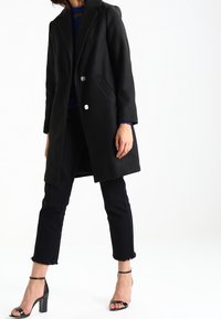 Sort uldblandingsfrakke med dobbeltknaplukning, sidelommer og et rent silhuet. Sammen med sorte cropped jeans og hæle.