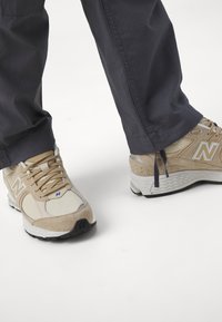 Beige New Balance Sneakers aus Mesh und Wildleder, ausgestattet mit einer weißen Sohle, grauen Akzenten und sichtbarem Branding an den Seiten.