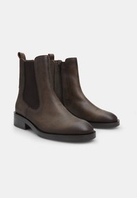 Botas chelsea de cuero marrón con paneles laterales elásticos y una cremallera discreta. Textura suave y punta redondeada, con un tacón bajo en bloque.