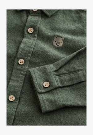 Grøn uldskjorte med knap-ned design, beige knapper og et lille broderet bjørnelogo på venstre bryst. Blød tekstur.