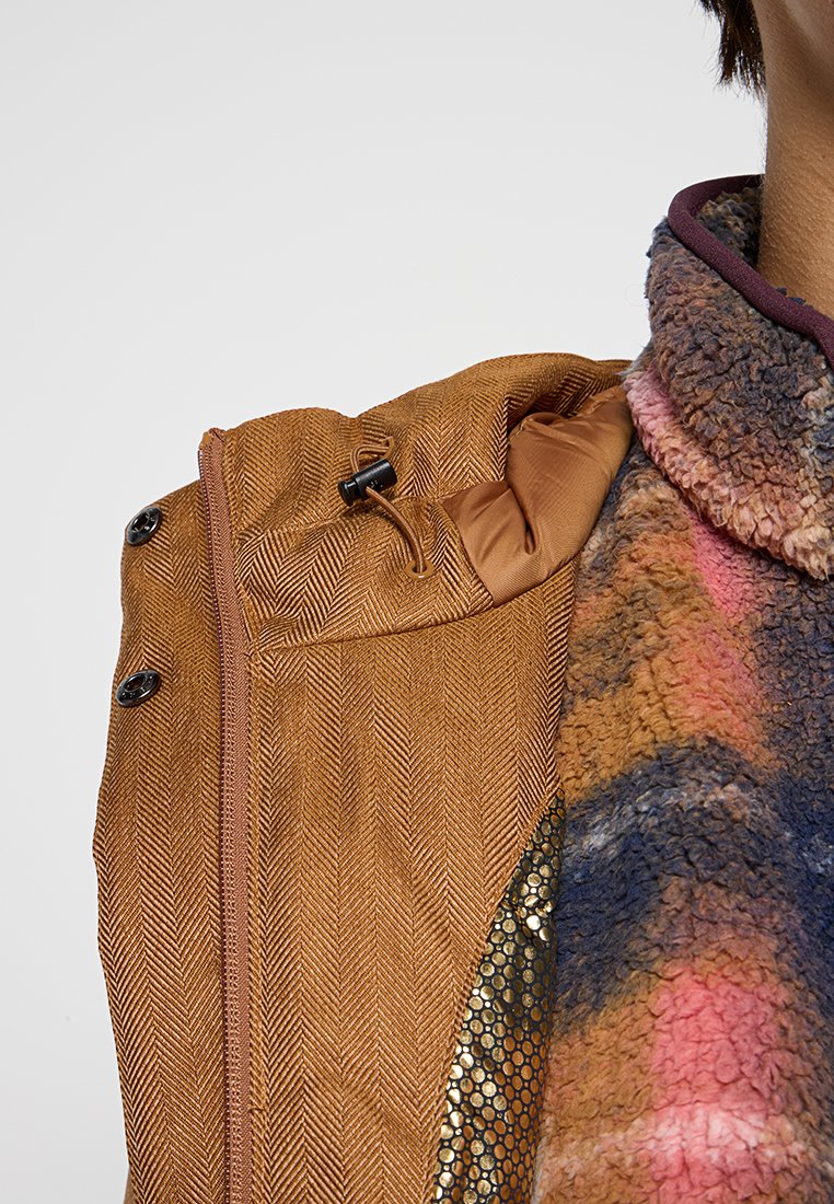 Braune Fischgrätenjacke mit strukturiertem Kragen, gepolstertem Kapuzenzug, Druckknöpfen und einem glänzenden Musterakzent an der Seite.