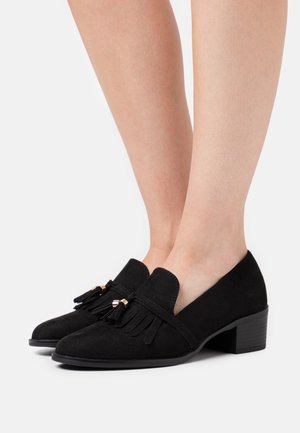 Mocassins en suède noir avec un petit talon carré, ornés de pampilles décoratives et d'accents dorés à l'avant pour plus de détails.