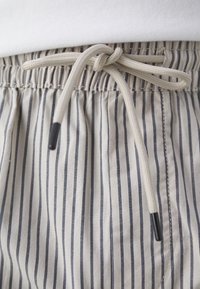 Cordon noué en nœud sur un pantalon beige et bleu marine à rayures verticales avec extrémités noires.
