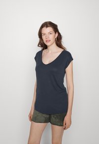 T-shirt azul-marinho de manga curta com decote em V, feito de um tecido suave, apresentando um corte descontraído. Usado com calções verde-oliva.