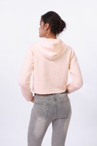 Sweatshirt cropped en rose clair avec un motif en chevrons et une capuche, associé à un jean en denim gris avec poches arrière et une légère décoloration.