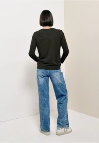 Schwarzes Langarmshirt, hellblaue lockere Jeans, lässige Sneakers. Glatter Stoff, lockere Passform, schlichtes Design. Von hinten gesehen.