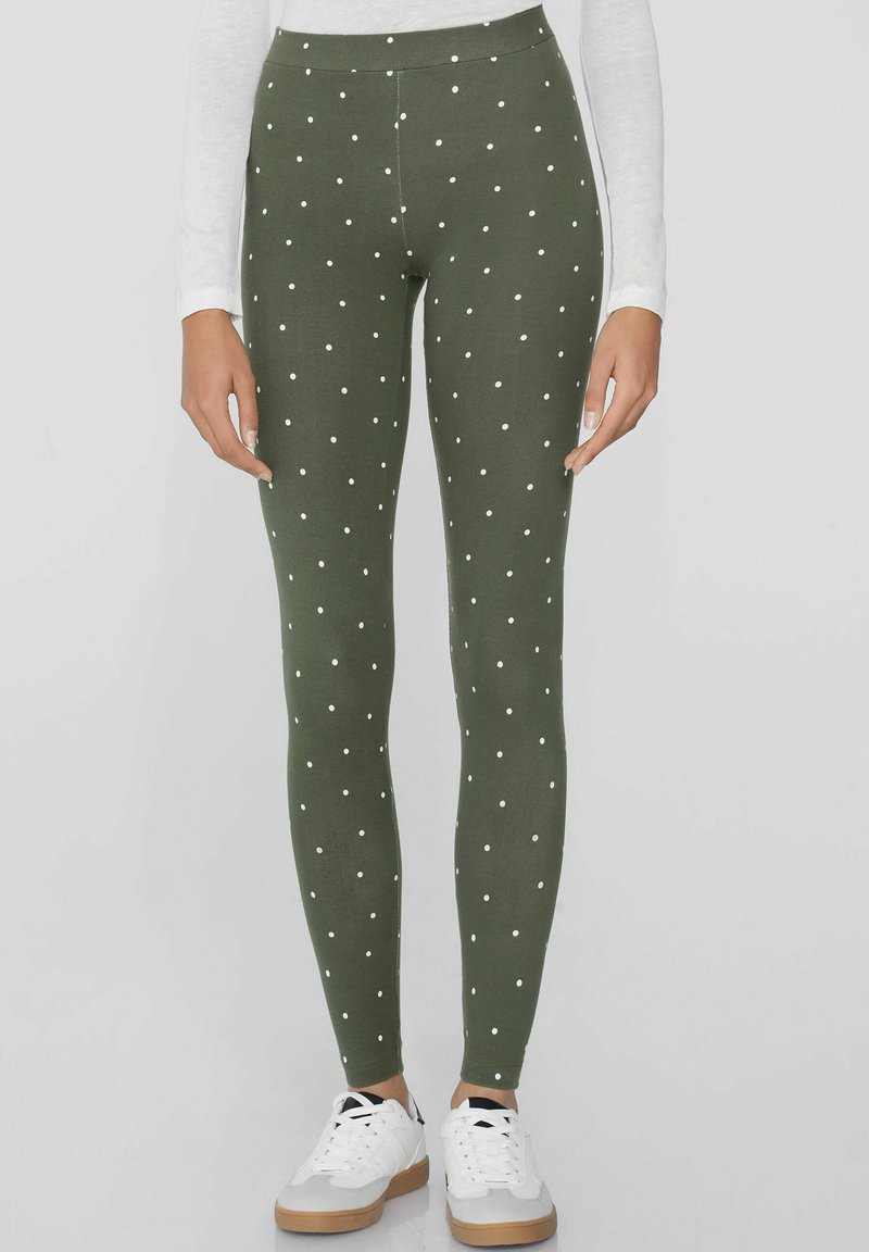 Leggings verts avec un motif de pois blancs sur toute la surface, fabriqués à partir d'un tissu extensible et doux. Associés à des baskets blanches.