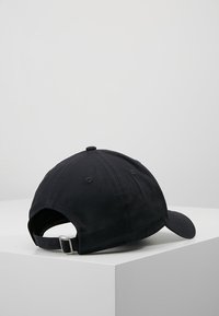 Black cotton baseball cap with a curved brim, adjustable metal strap at the back, and stitched ventilation holes.
